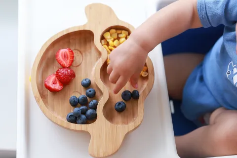 Plato de frutas y verduras con mano de bebé comiendo