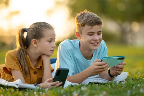 Niña y niño jugando con teléfonos móviles en el pasto
